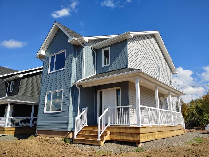 Brand new fully finished 2 story house light blue siding, wrap-around porch, and white door and railing.